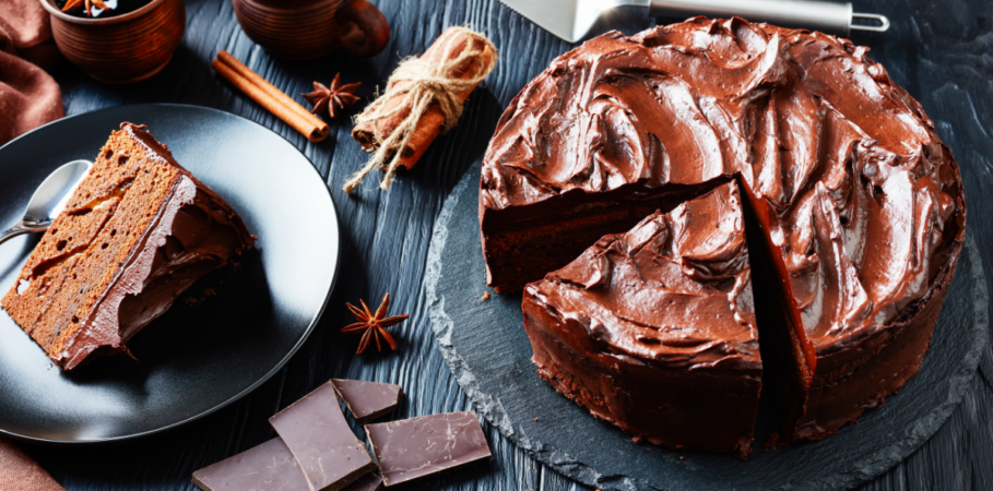 Professional chocolate cake with pieces of chocolate bars, spices, and a slice of cake on black plates and a black table.