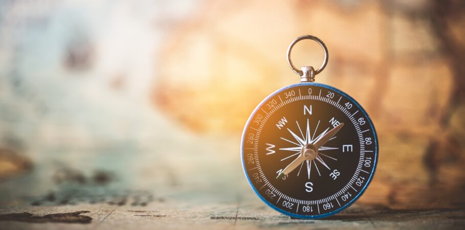 Black and white compass that’s been set upright on a desk with a faded globe in the background, symbolizing the best CCMS guidance.